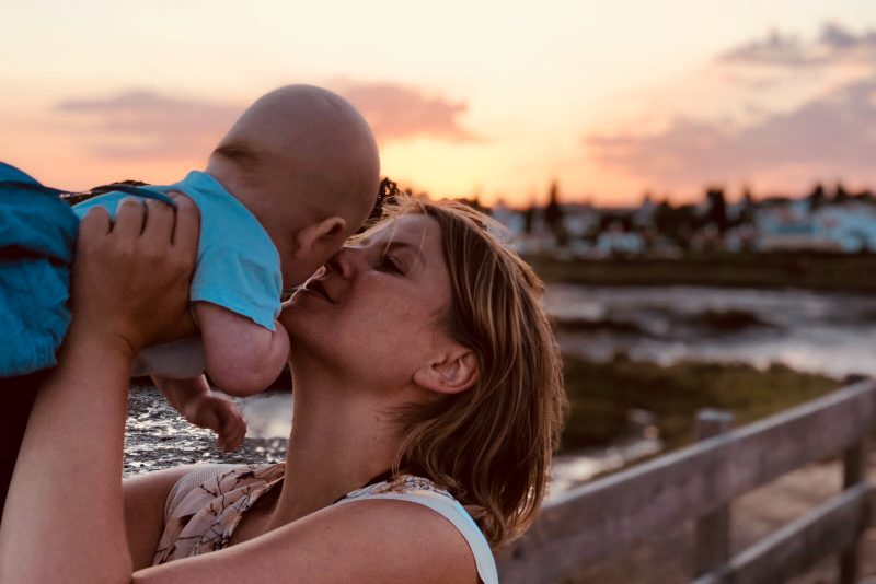 Mama küsst Baby im Sonnenuntergang